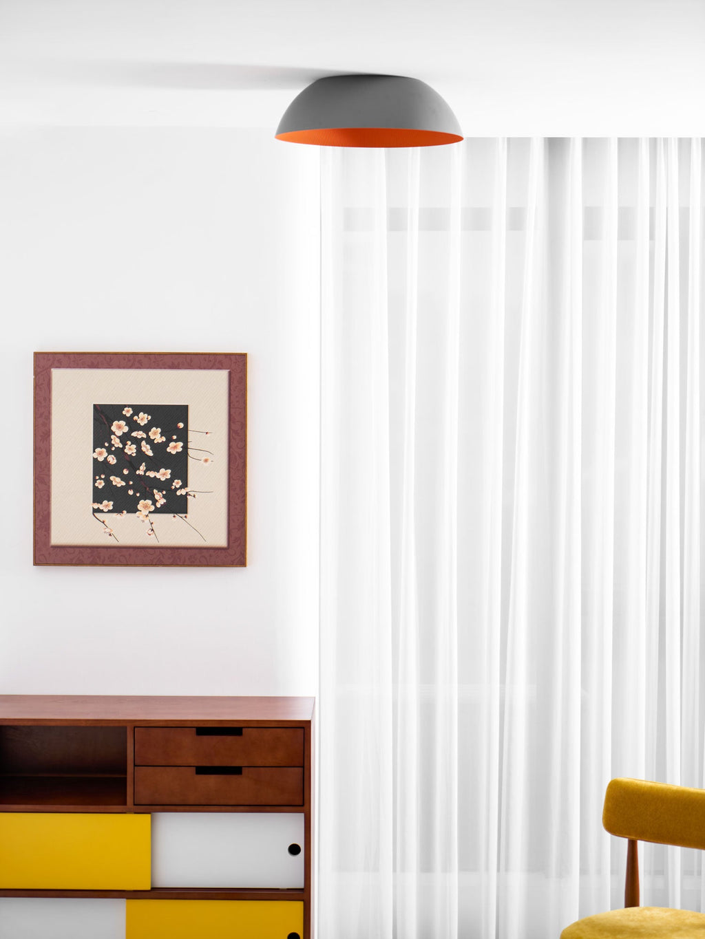Grey dome ceiling light from Clérachic viewed from the side, above a white room with a framed print and a yellow sideboard.