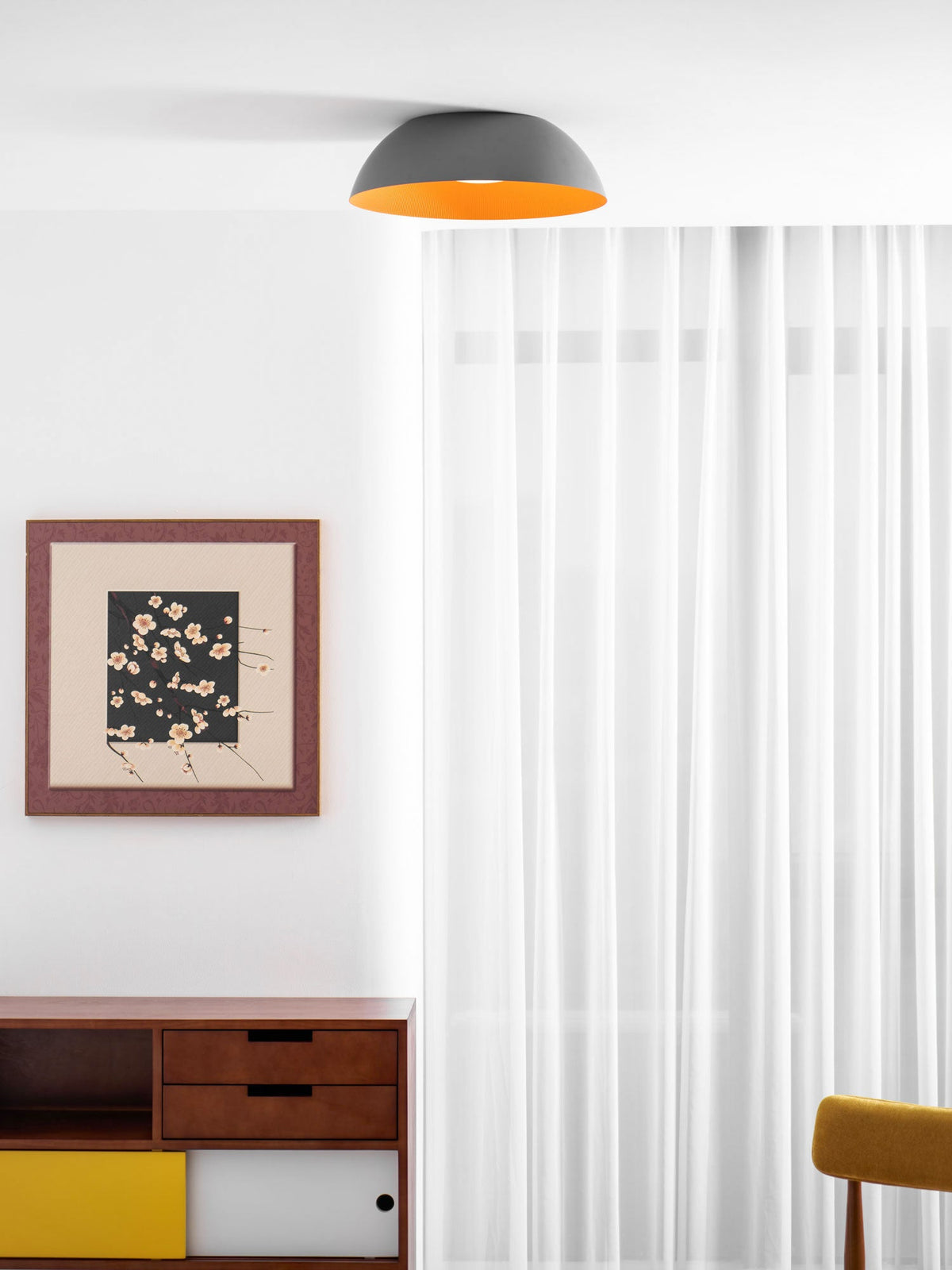Grey dome ceiling light with a thin orange edge, from Clérachic, above sheer curtains and a mid-century sideboard.