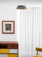 Grey Clérachic dome ceiling light seen almost edge-on above a white room with sheer curtains, a framed print and a yellow chair.