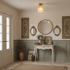 This Clérachic ceiling light lights a hall with a round gold mirror, small oval mirrors, tapestries and a white console on sage panelling.