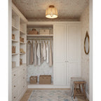 A Clérachic ceiling light with a linen shade in a narrow dressing room with white cupboards, floral wallpaper and a wooden stool.