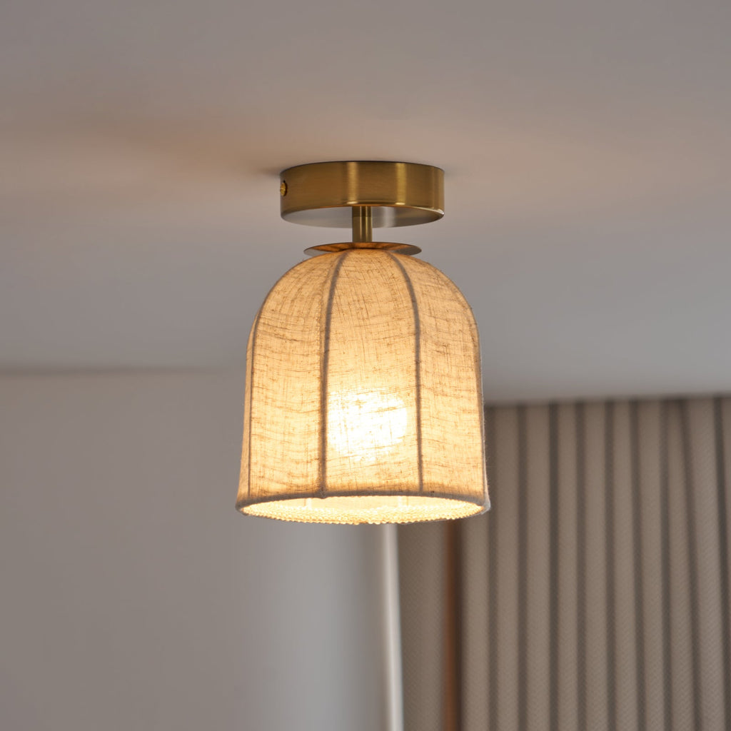 Close view of this Clérachic ceiling light lit warm, with a ribbed linen shade, a gold canopy and a beaded trim at the rim.