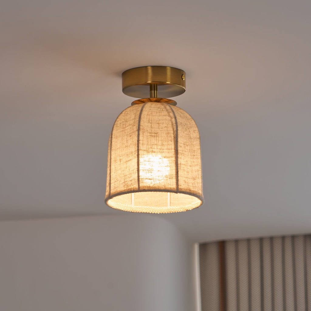 A Clérachic flush-mount light with a lit linen shade and gold canopy, seen from slightly below against a soft grey ceiling.