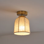 Smaller Clérachic ceiling light glowing warm, with its linen shade and gold canopy set against a plain grey ceiling.