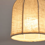 Close view of the woven linen weave and the fabric ribs on this lit Clérachic ceiling light, with a soft warm glow behind.