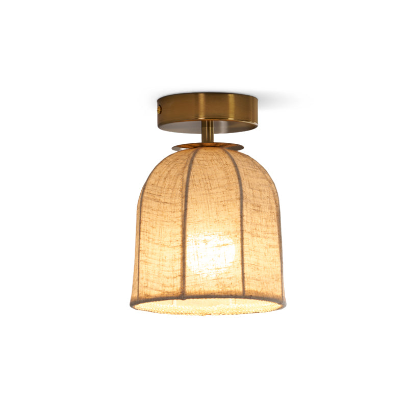 A lit Clérachic flush-mount light on a white backdrop, its ribbed linen shade glowing amber under a gold canopy.