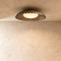 Clérachic ceiling light in vintage brass, a shallow perforated drum haloed with warm light on a plaster ceiling.