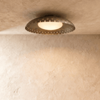 Clérachic ceiling light in vintage brass, a shallow perforated drum haloed with warm light on a plaster ceiling.