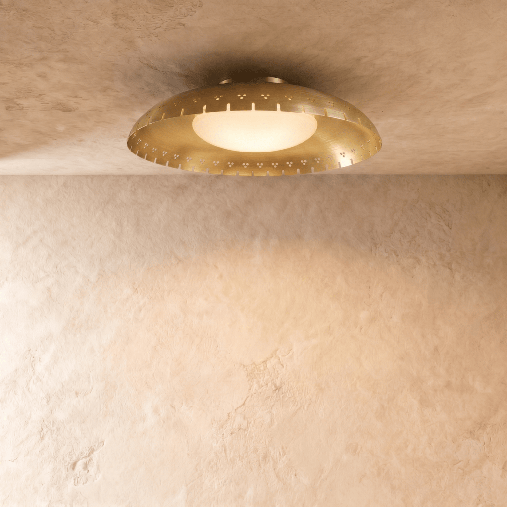 Clérachic ceiling light in brushed brass, the perforated drum shade casting a warm halo on the ceiling.