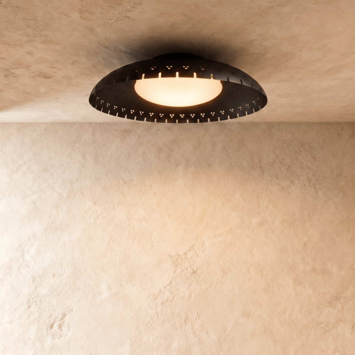 Clérachic ceiling light in matte black, a shallow perforated drum glowing warmly against a plaster ceiling.