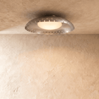 Clérachic ceiling light in chrome, its slotted metal rim reflecting soft light on a plaster ceiling.