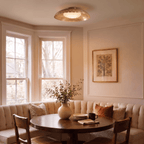 Clérachic ceiling light in brushed brass above a round table in a sunlit breakfast nook with bay windows.