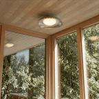 Clérachic ceiling light in chrome mounted in a wood-paneled sunroom overlooking a leafy garden view.