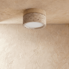 Clérachic ceiling light with a light wood band over a speckled travertine-look drum, glowing warm overhead.