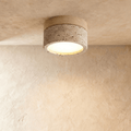Clérachic ceiling light in light wood and travertine-look stone, glowing warm from the flush drum shade.