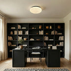 A Clérachic ceiling light with a black rim sits above a black desk and open black bookcase in a home study.