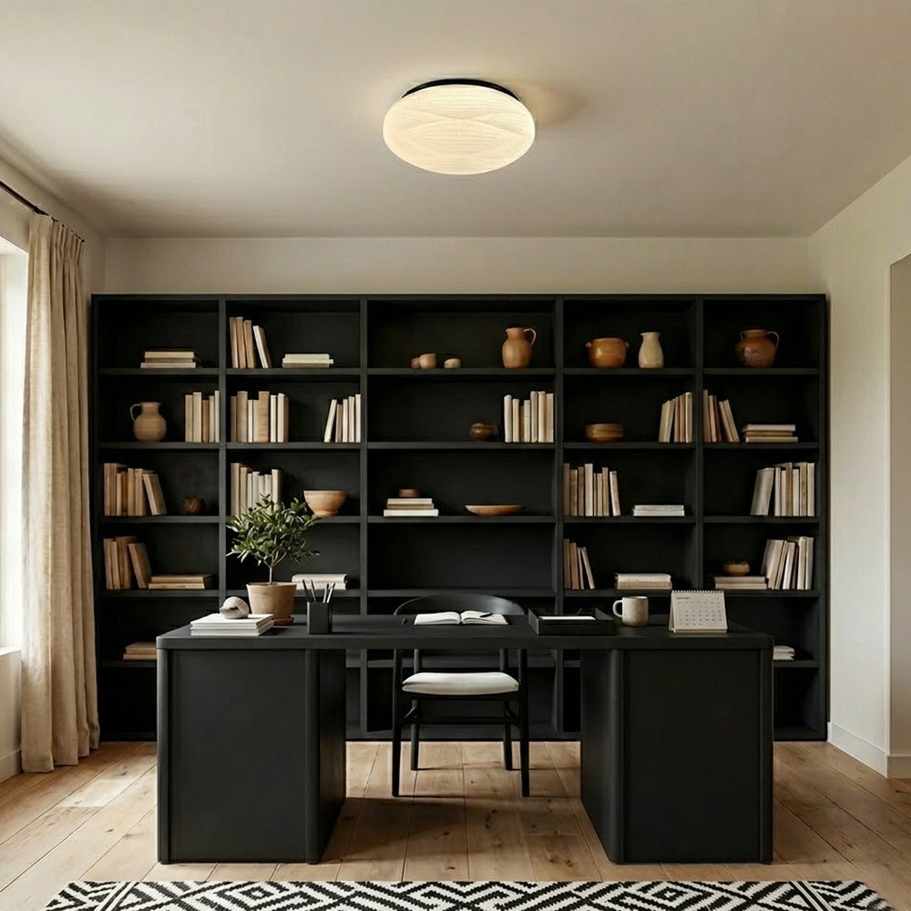 A Clérachic ceiling light with a black rim sits above a black desk and open black bookcase in a home study.