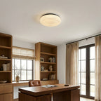A round Clérachic ceiling light with a dark rim glows above a wooden desk, with open shelving and French doors behind.