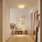 A small Clérachic ceiling light lights a bright entrance hall with a woven bench, framed prints and a leaning floor mirror.