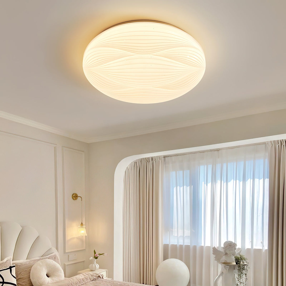 Close view from below of this Clérachic ceiling light lit, its ribbed shade showing woven curved lines above a white bedroom.