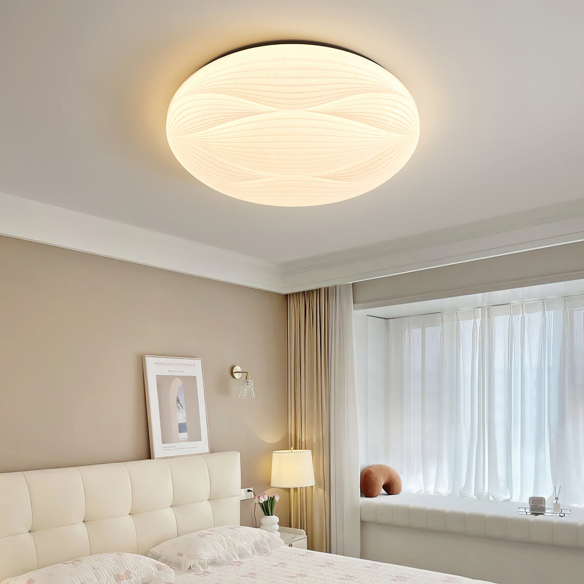 A wide, lit Clérachic ceiling light with a black rim above a tufted cream bed and a window seat.