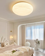 Gold-rimmed Clérachic ceiling light lit in an arched bedroom alcove, with a throw blanket and a small statue below.