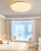 A lit Clérachic ceiling light with a gold rim in a bedroom with a tall window, a window seat and a laptop on the bed.