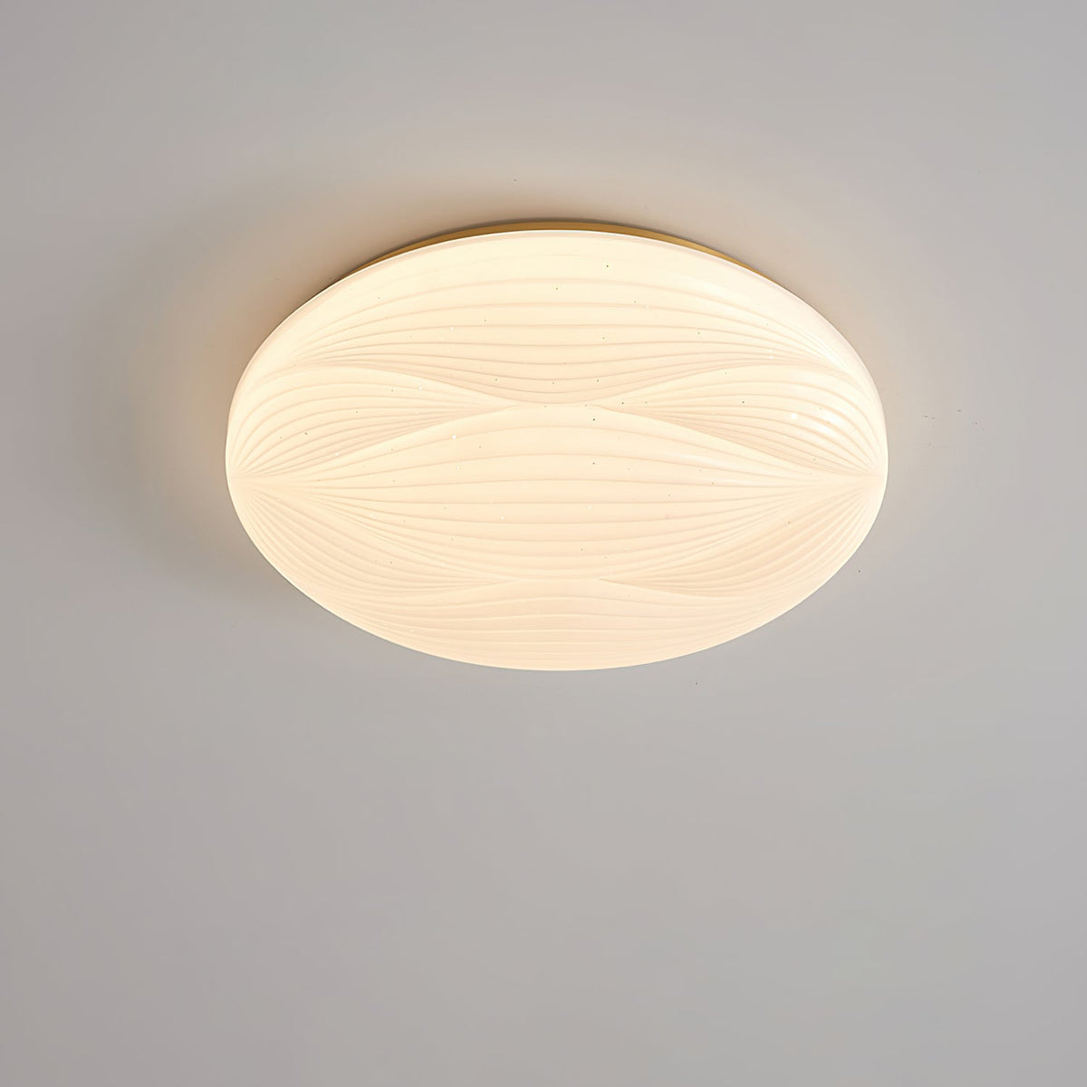 Looking up at this Clérachic ceiling light, its gold rim and wavy ribbed shade lit softly against a grey ceiling.