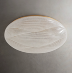 A textured translucent shade with fine wave ribs and a gold rim, on this unlit Clérachic ceiling light against a dark grey wall.