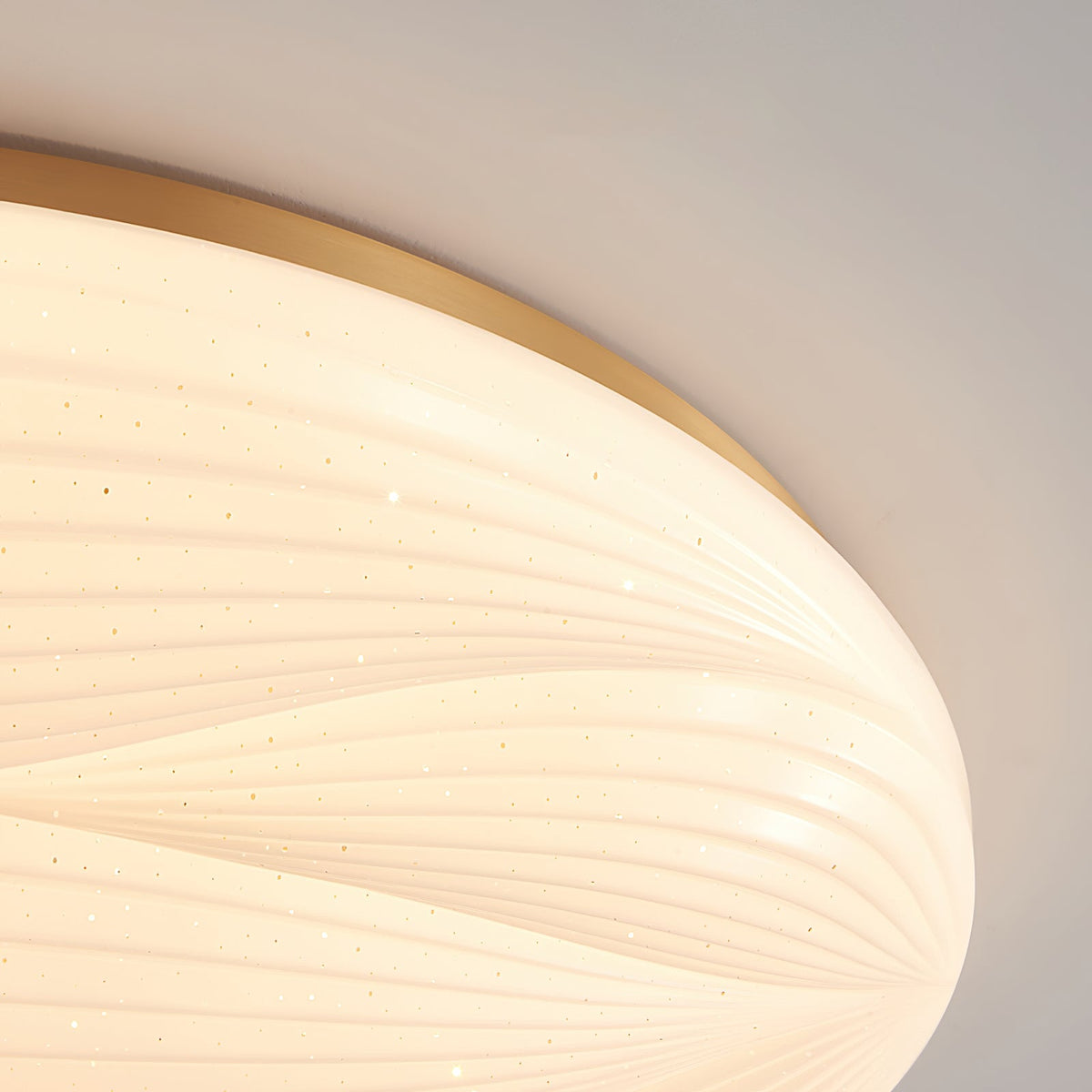 Close view of the gold rim and finely ribbed glowing shade of this Clérachic ceiling light, with tiny pin-point sparkles.