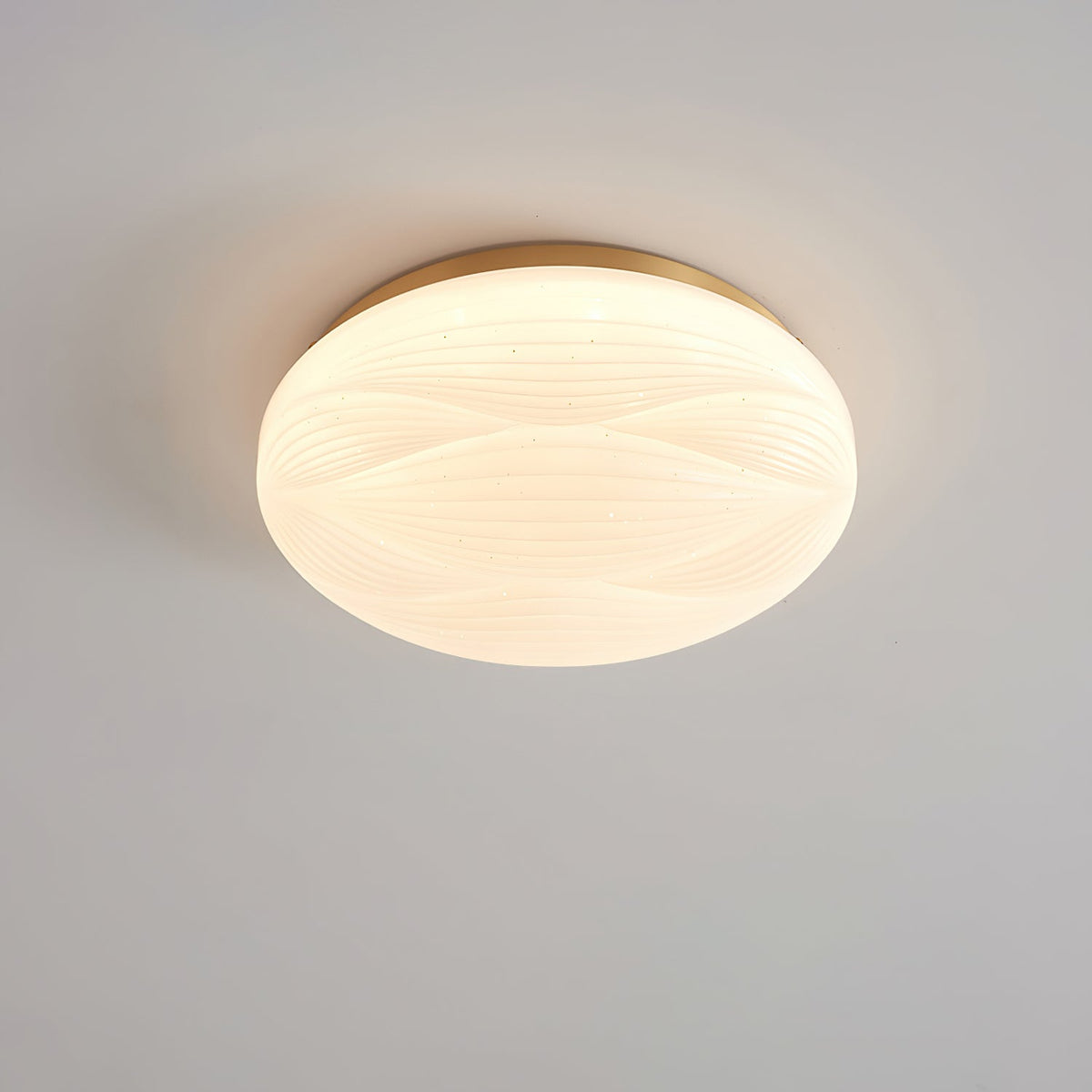 Small, lit Clérachic ceiling light with a gold rim and a milky ribbed shade against a grey ceiling.