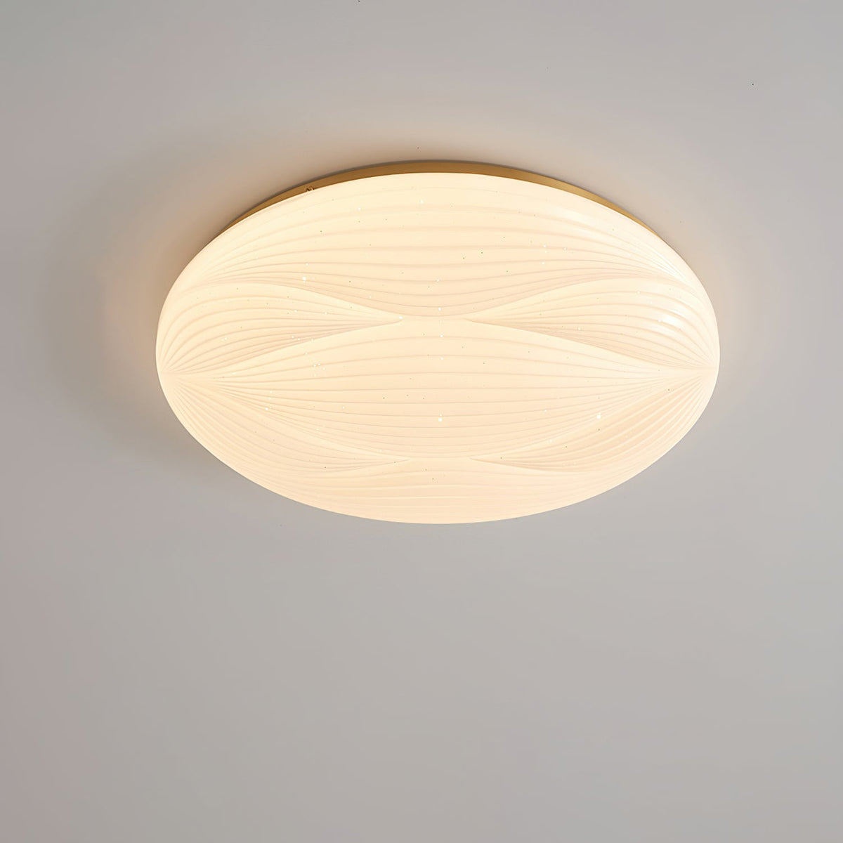 A larger lit Clérachic ceiling light with a gold rim, its milky shade showing curved ribs, on a grey ceiling.