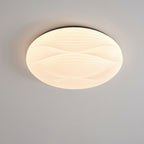 A wider Clérachic ceiling light with a black rim glows with a ribbed white shade against a grey ceiling.