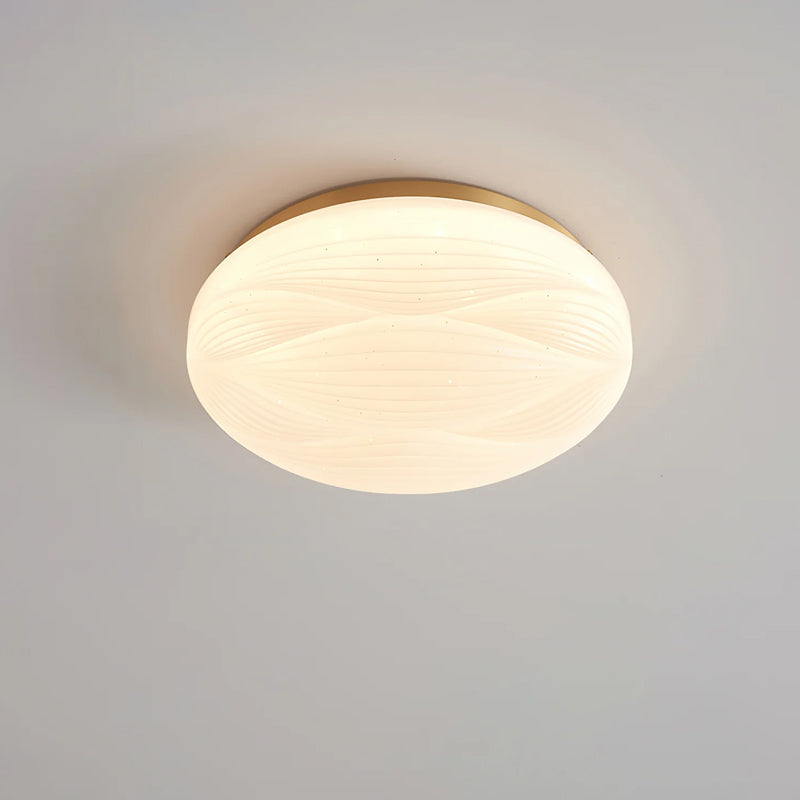 A gold-rimmed Clérachic ceiling light lit against a grey ceiling, with a soft white ribbed shade.