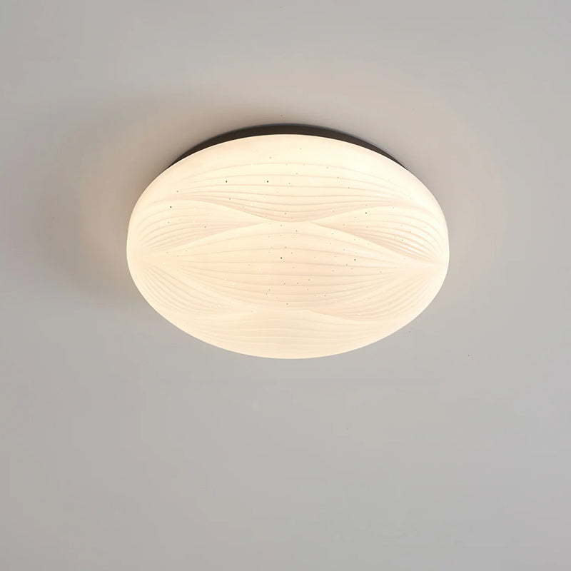 Lit Clérachic ceiling light with a black rim and a softly ribbed white shade, seen from the side on grey.