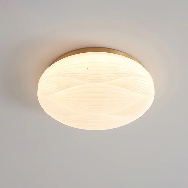 Close angle on a lit, gold-rimmed Clérachic ceiling light with its deeper ribbed white shade on a grey ceiling.