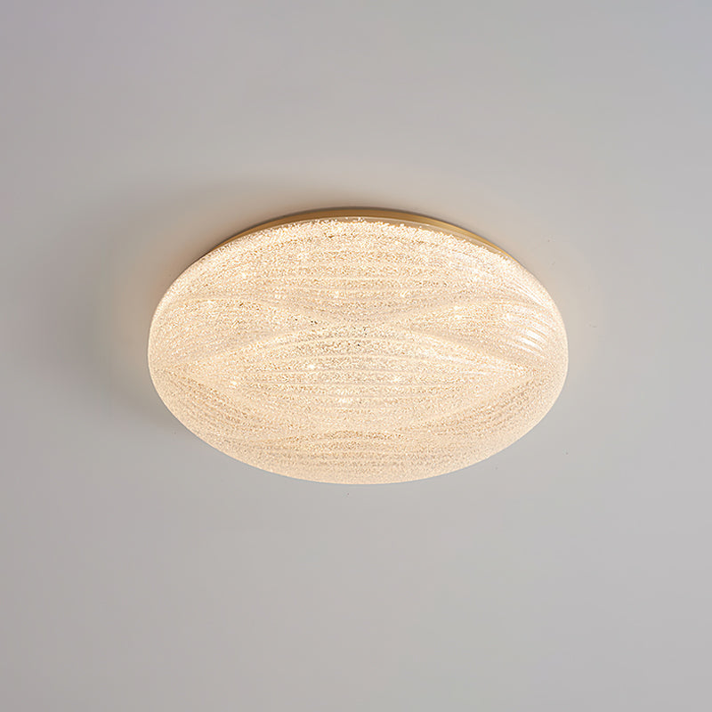 Lit Clérachic ceiling light with a gold rim and a sparkly, crystal-textured shade on a grey ceiling.
