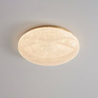 A lit Clérachic ceiling light with a gold rim, its textured shade giving off a warm, glittering glow.