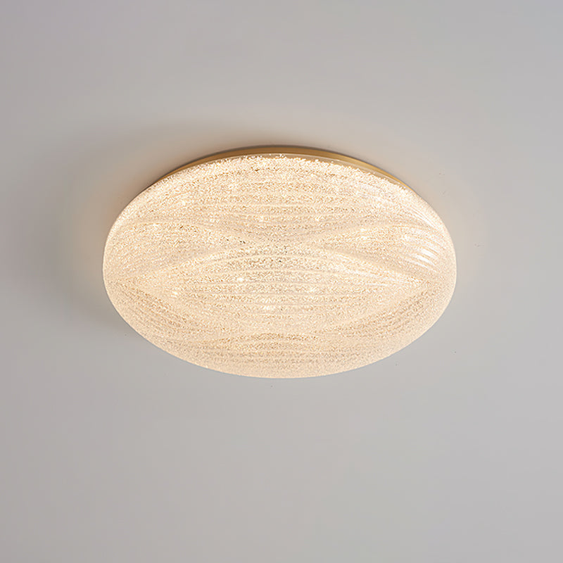 A lit Clérachic ceiling light with a gold rim, its textured shade giving off a warm, glittering glow.