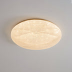A wider gold-rimmed Clérachic ceiling light lit with a glittering textured shade against a grey ceiling.