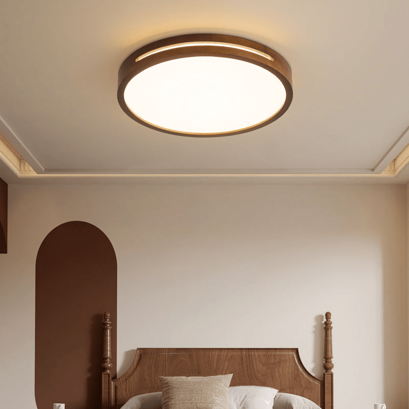 Lit round walnut-frame ceiling light from Clérachic above a carved wooden bed in a calm bedroom with an arched brown wall panel.