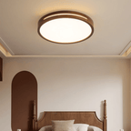 Lit round walnut-frame ceiling light from Clérachic above a carved wooden bed in a calm bedroom with an arched brown wall panel.
