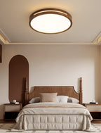 A round walnut-frame Clérachic ceiling light lit above a carved headboard bed, with rattan bedside tables on each side.