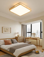 Square Clérachic ceiling light with a pale wood frame glowing in a bedroom with a dressing table and a window beyond.