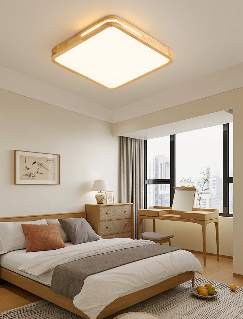 Square Clérachic ceiling light with a pale wood frame glowing in a bedroom with a dressing table and a window beyond.