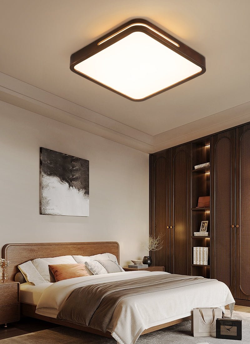 Square walnut-frame ceiling light from Clérachic above a bed with a brown throw, beside tall dark wooden wardrobes.