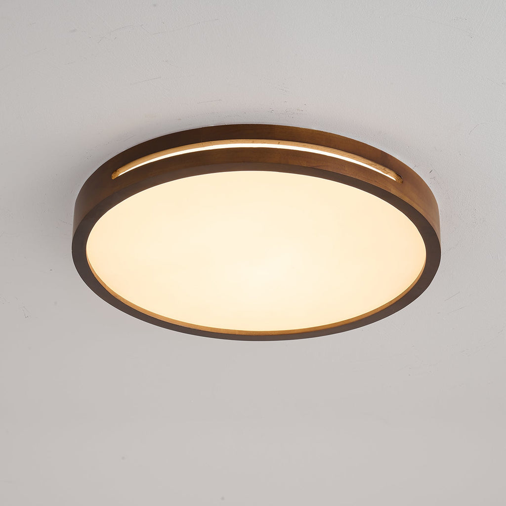 Round walnut-frame Clérachic ceiling light lit warm against a grey ceiling, with a soft glow across the frosted panel.