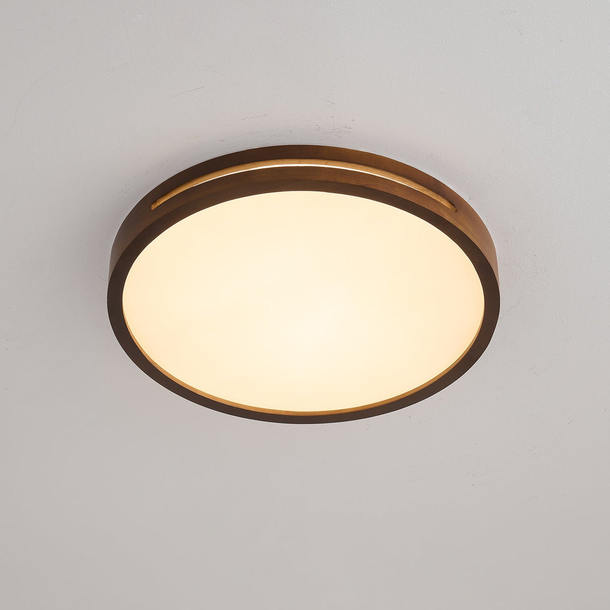 Round dark walnut ceiling light from Clérachic with a warm glow behind its frosted panel, photographed on a grey ceiling.