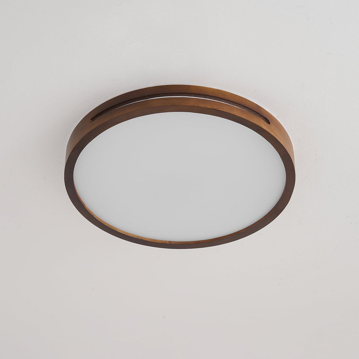 Round walnut-frame ceiling light from Clérachic, unlit, with a slotted wood rim around a flat frosted panel.