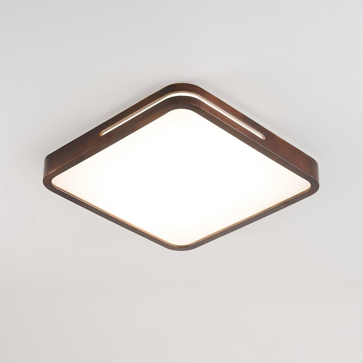 Square walnut-frame Clérachic ceiling light lit in a bright, neutral white, with its slotted rim visible on one side.